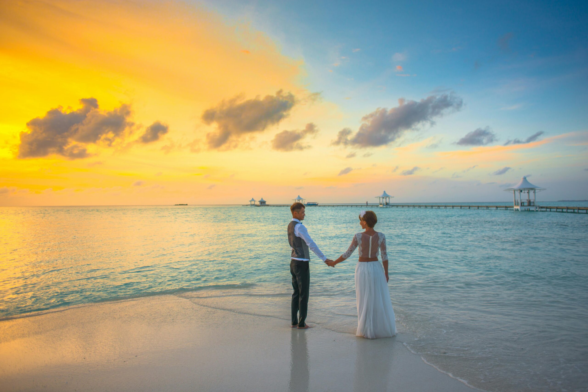 White floral ceremony arch on a tropical beach at sunset