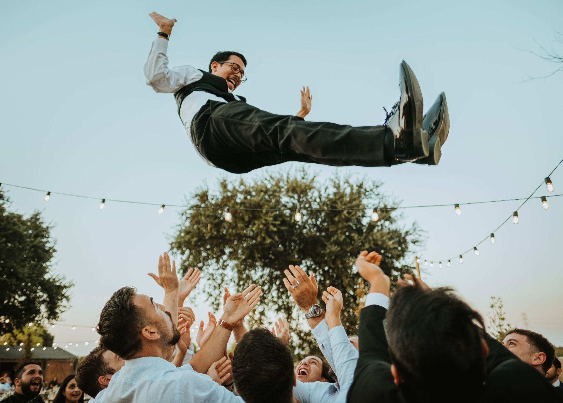Friends lifting the groom in the air during an outdoor wedding celebration