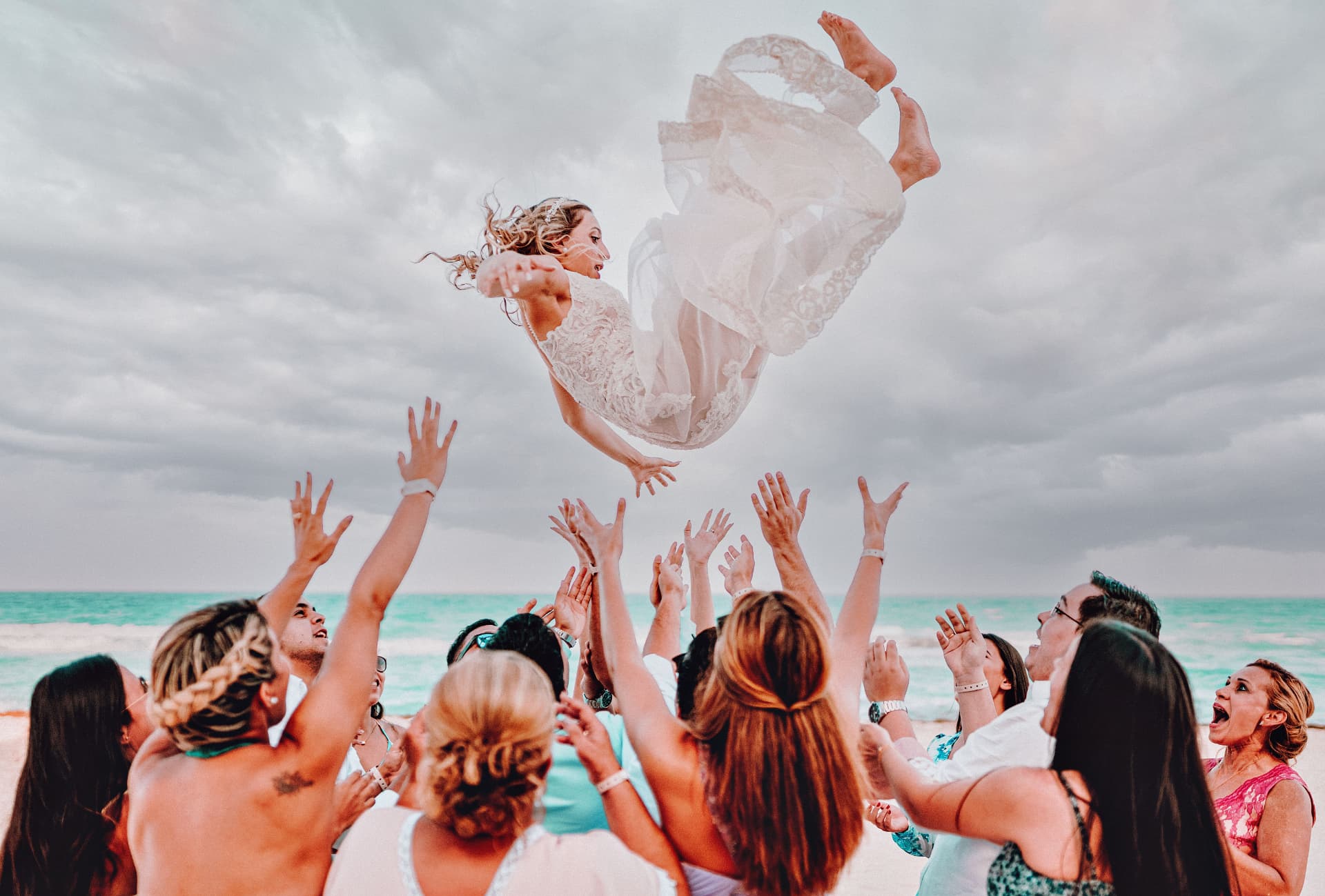 Guests tossing the bride in the air on the beach during a destination wedding room block celebration